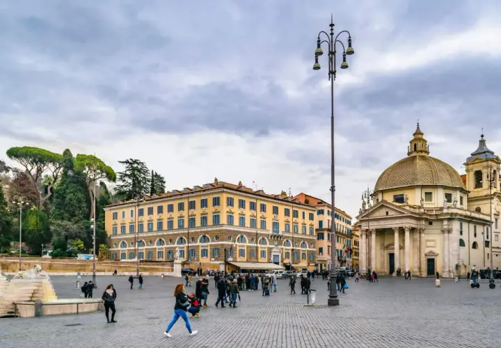 Piazza del Popolo a Roma a novembre, con la chiesa gemella e il palazzo giallo sotto un cielo nuvoloso.