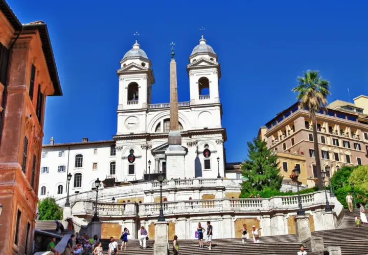 La scalinata di Trinità dei Monti a Roma, con la chiesa e l'obelisco sotto un cielo azzurro.