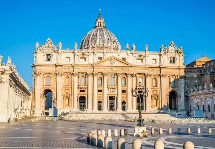 La maestosa basilica di San Pietro, un'antica meraviglia architettonica, domina la piazza con la sua imponente cupola sotto un cielo azzurro.