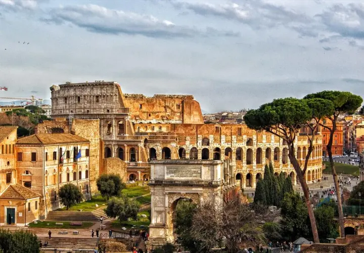 Colosseo e Arco di Tito, un'idea di cosa vedere a Roma in un giorno gratis, con pini romani e cielo nuvoloso.