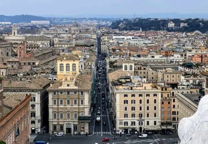 Vista aerea di Roma con traffico su Via del Corso. Edifici storici e tetti si estendono all'infinito.