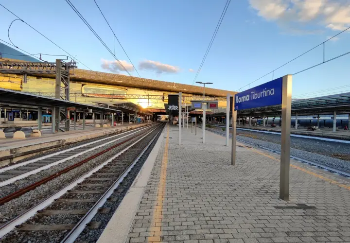 Binari e pensiline alla stazione Roma Tiburtina, con il sole che illumina la moderna architettura.
