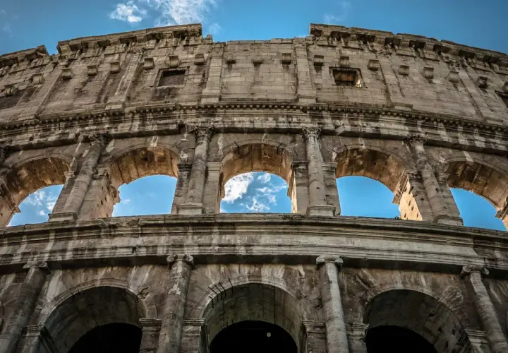 Il Colosseo visto dal basso, con il cielo azzurro e nuvole tra gli archi. Un'ottima meta per chi cerca come arrivare al Colosseo da Stazione Termini.
