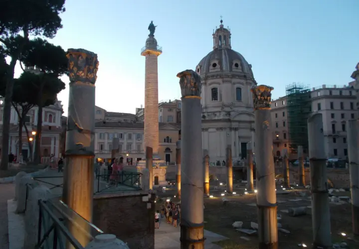 Antiche colonne onorarie illuminate di sera, con una cupola sullo sfondo.