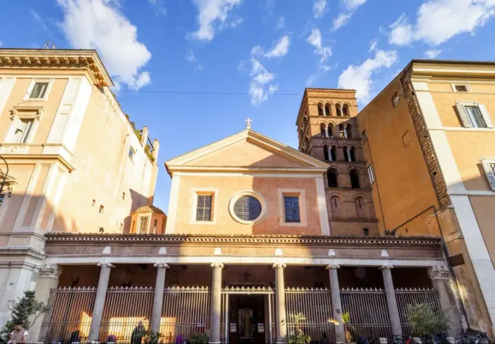 Facciata di San Lorenzo in Lucina a Roma, con il suo campanile romanico e palazzi circostanti sotto un cielo azzurro con nuvole bianche.