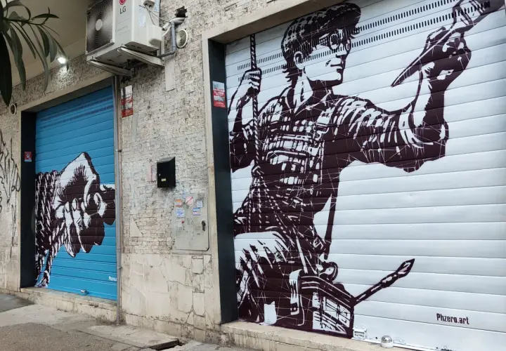 Un pugno su saracinesca blu e un artista al lavoro su un altro saracinesca: arte urbana in un quartiere murales di Roma.
