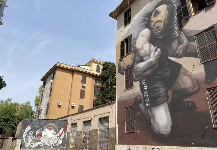 Street art a Tor Marancia: un imponente murale raffigura un lottatore con maschera tribale, mentre su un muro più basso un'altra opera celebra la cultura orientale.