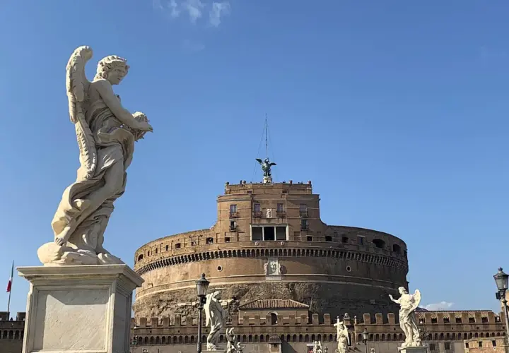 Un angelo scolpito domina la scena davanti al maestoso mausoleo di Roma, Castel Sant'Angelo, sotto un cielo azzurro.