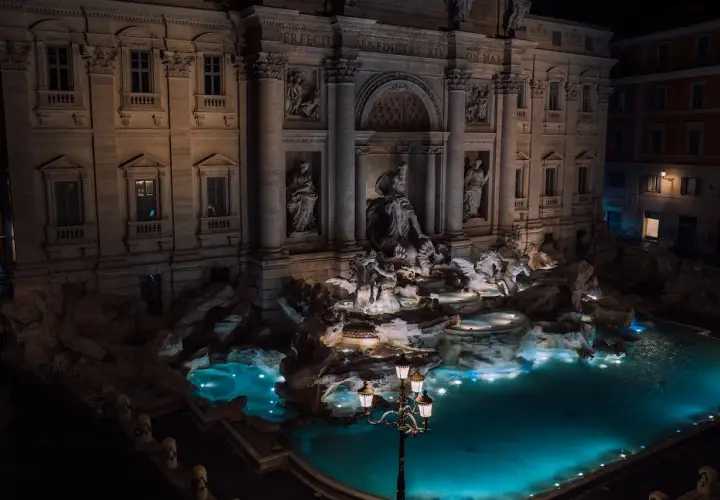 Fontana di Trevi a Roma di notte, con le sue sculture illuminate e l'acqua turchese che brilla sotto i lampioni.