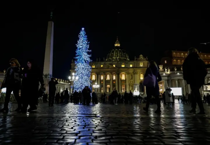 Piazza San Pietro illuminata da un grande albero di Natale blu, con gente che passeggia. Un'idea su cosa fare il 24 dicembre a Roma.