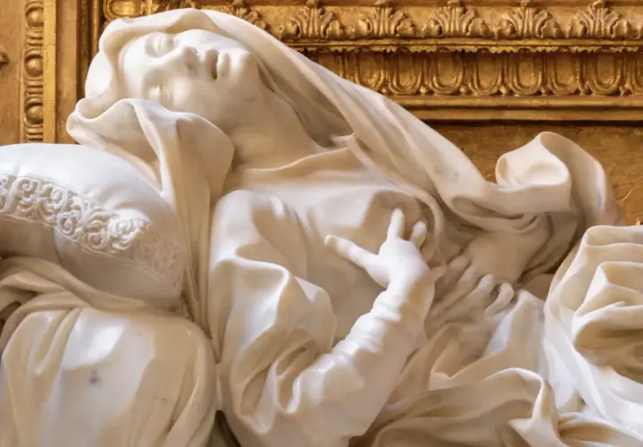 Estasi di Santa Teresa a Roma, marmo bianco su fondo dorato. La santa giace su un cuscino, con un'espressione di profonda emozione.