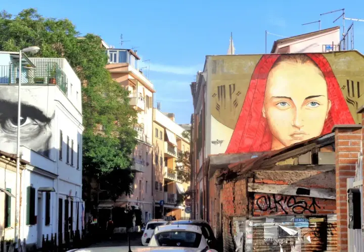 Un grande volto femminile con un velo rosso domina un edificio nel quartiere Pigneto. Accanto, un occhio gigante osserva la strada.