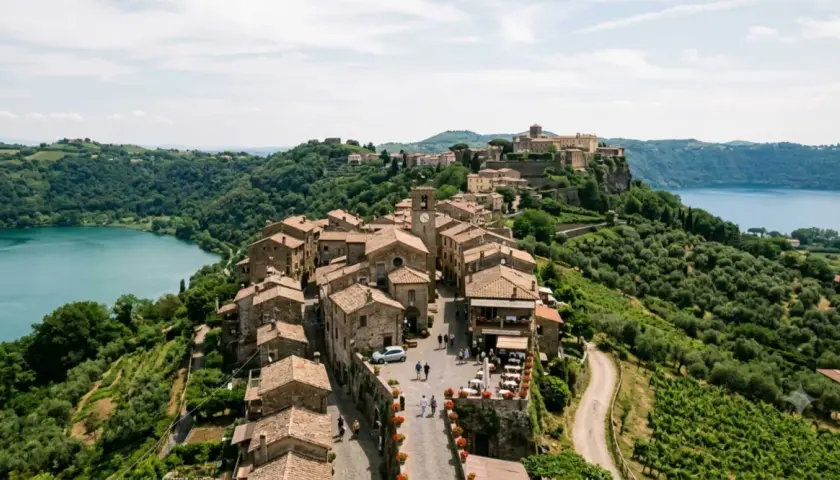 Borgo medievale sui Colli Albani, con case in pietra, un lago azzurro e uliveti rigogliosi.