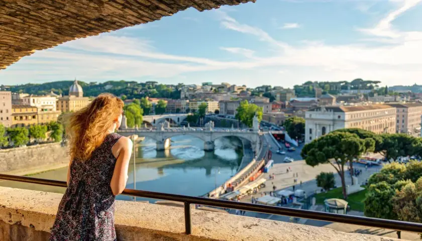 Una donna ammira il panorama di Roma con il Tevere e Ponte Sant'Angelo, un'immagine perfetta per il Ferragosto a Roma.