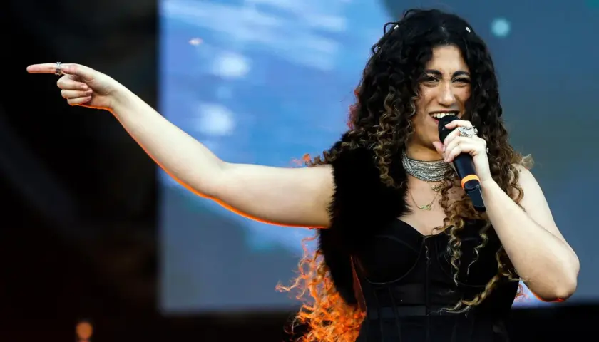 Una delle tanti artisti primo maggio, canta con passione sul palco, indicando il pubblico con un gesto energico.