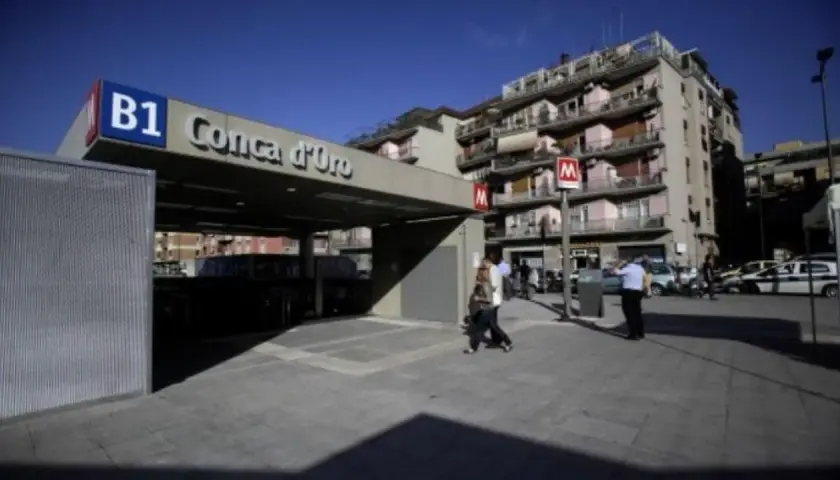 Ingresso della metro B1 Conca d'Oro a Roma, con persone che camminano e palazzi sullo sfondo.