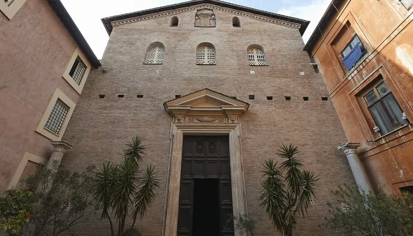 Facciata in mattoni di Santa Prassede a Roma, con un grande portale in legno e piante verdi.