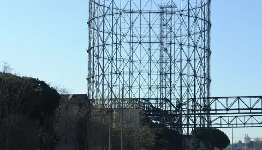 Il **gasometro Roma** si erge imponente contro il cielo azzurro, una struttura metallica iconica che domina il paesaggio urbano.