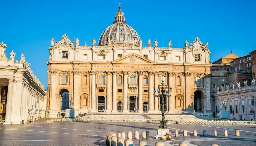 La maestosa basilica di San Pietro, un'antica meraviglia architettonica, domina la piazza con la sua imponente cupola sotto un cielo azzurro.