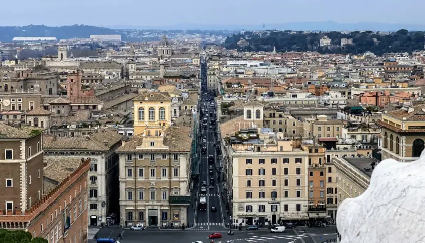 Vista aerea di Roma con traffico su Via del Corso. Edifici storici e tetti si estendono all'infinito.