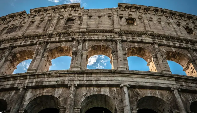 Il Colosseo visto dal basso, con il cielo azzurro e nuvole tra gli archi. Un'ottima meta per chi cerca come arrivare al Colosseo da Stazione Termini.