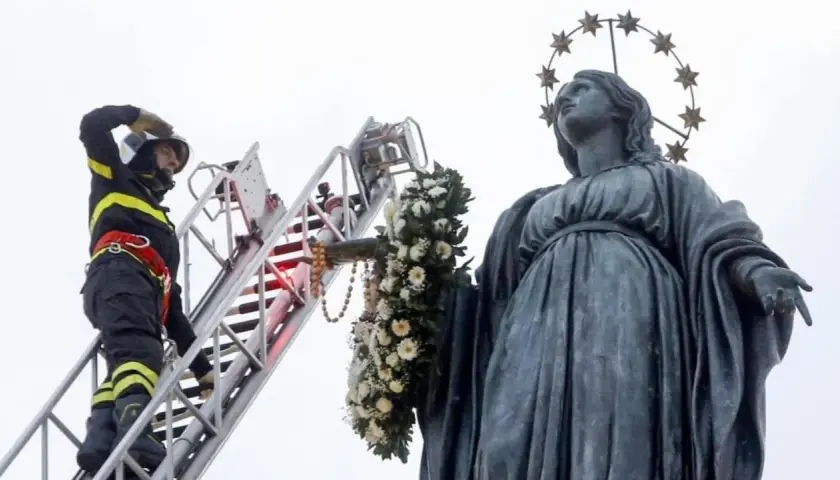 Vigile del fuoco su scala decora la statua della Madonna con fiori per l'8 dicembre a Roma.
