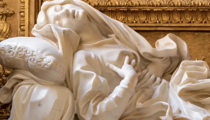 Estasi di Santa Teresa a Roma, marmo bianco su fondo dorato. La santa giace su un cuscino, con un'espressione di profonda emozione.