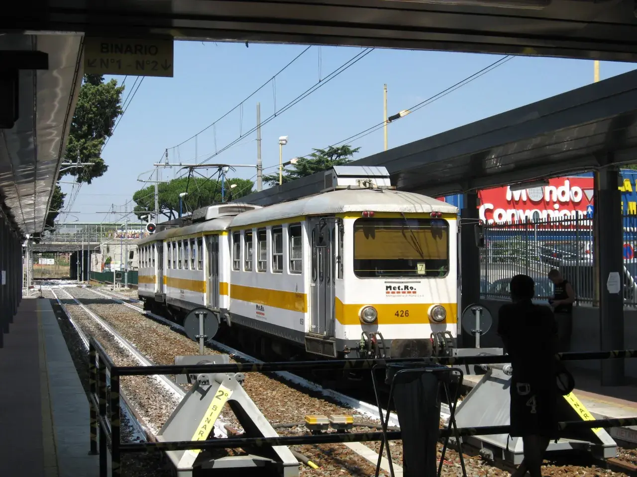 Treno della metro C a Torrenova, con segnale "Binario N°1 - N°2". Persone in attesa sul binario.