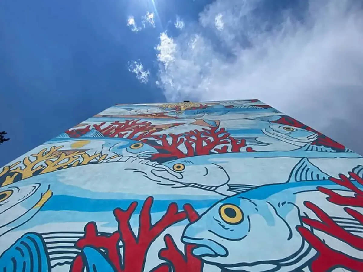 Un'onda di colori subacquei decora un muro a Roma, un'esplosione di vita marina e coralli rossi. Roma street art che porta il mare in città.