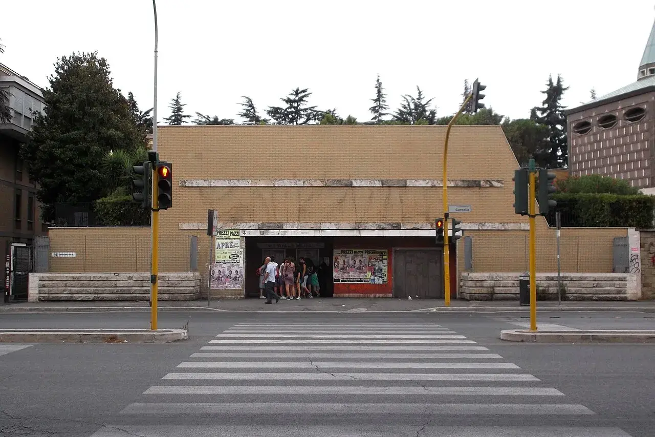 Ingresso della metro Cornelia a Roma, con persone in attesa e semafori rossi.