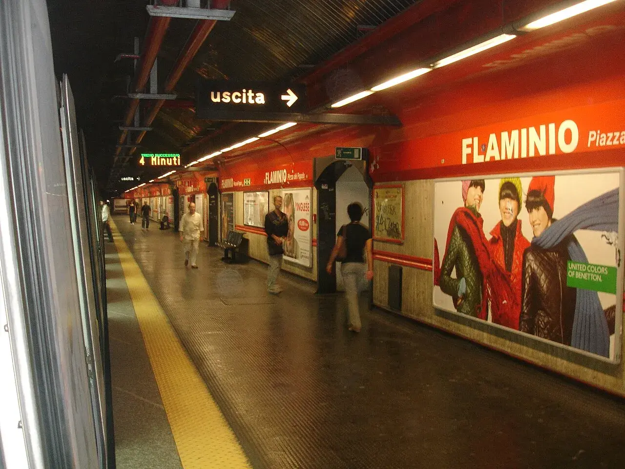 Stazione della metro Roma Nord, banchina con persone in attesa, cartelloni pubblicitari e indicazioni per l'uscita.