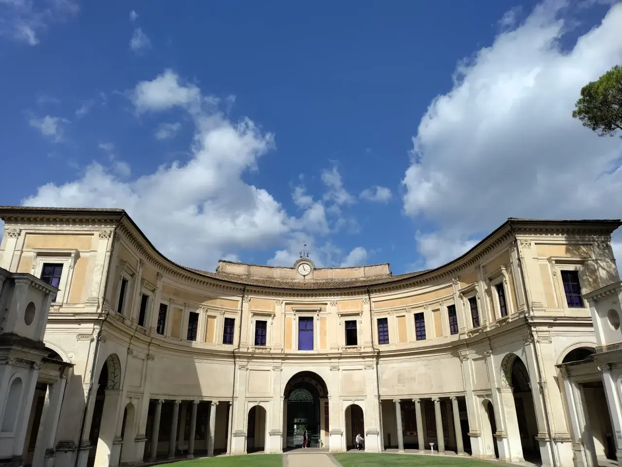 Cortile semicircolare di Villa Giulia a Roma, con un cielo azzurro e nuvole bianche.