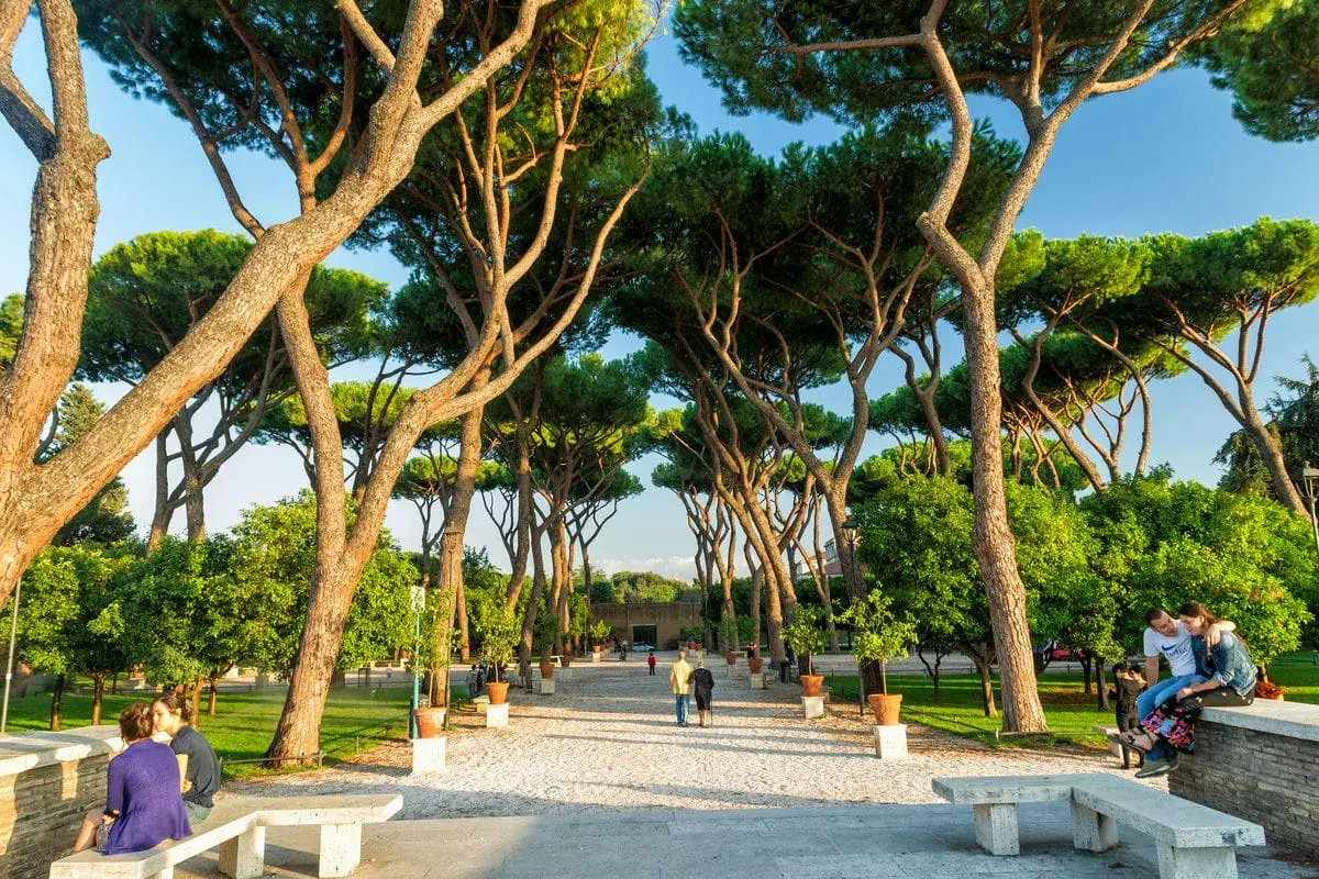 Passeggiata tra i pini marittimi nei giardini di Roma, con persone che si godono la tranquillità e il verde.
