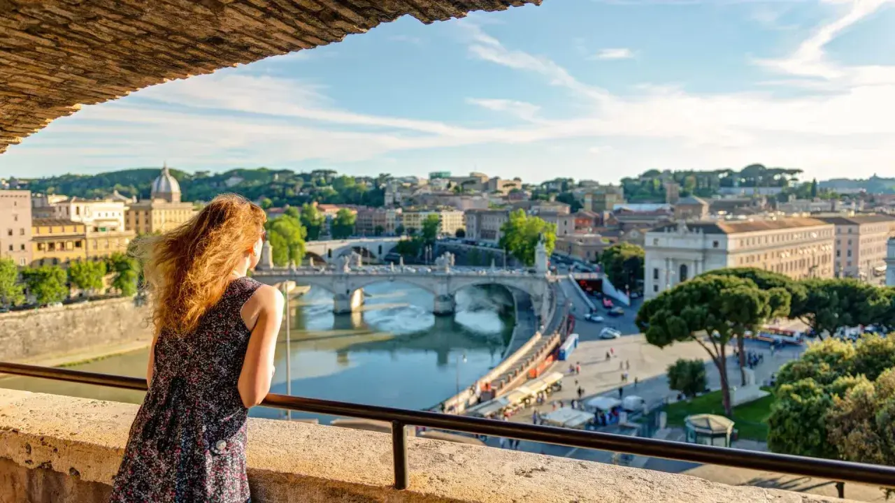 Una donna ammira il panorama di Roma con il Tevere e Ponte Sant'Angelo, un'immagine perfetta per il Ferragosto a Roma.