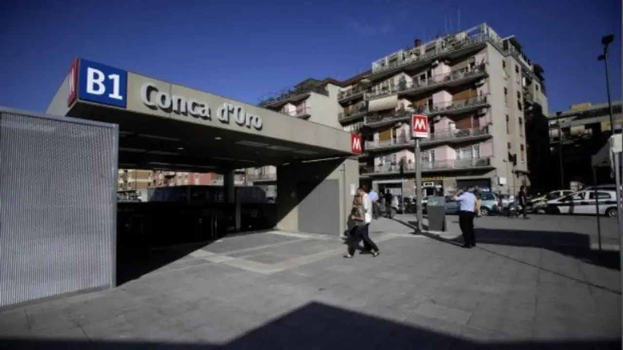 Ingresso della metro B1 Conca d'Oro a Roma, con persone che camminano e palazzi sullo sfondo.