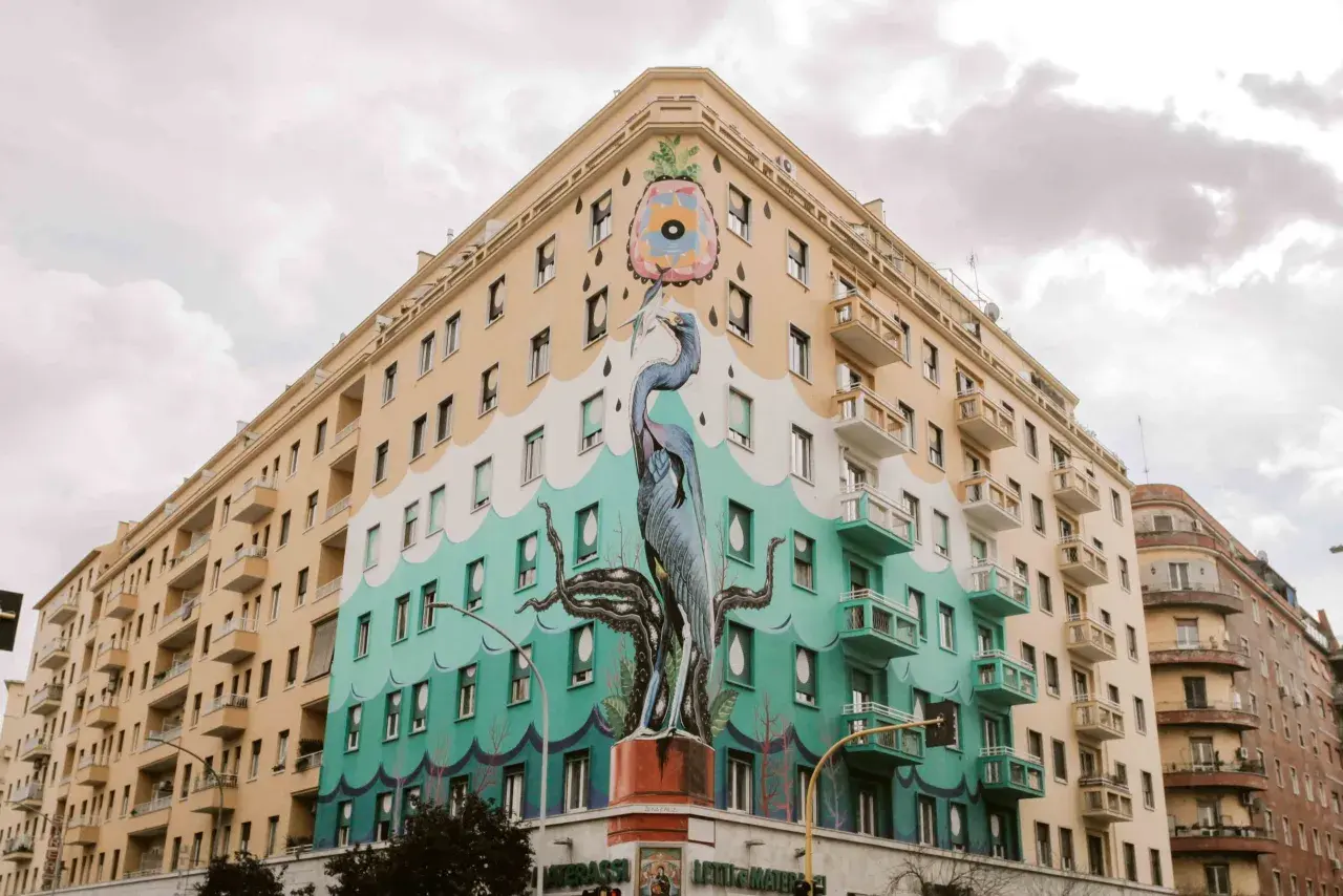 Un maestoso airone blu e tentacoli di polpo adornano un palazzo nel quartiere Ostiense, un'opera d'arte urbana che cattura lo sguardo.