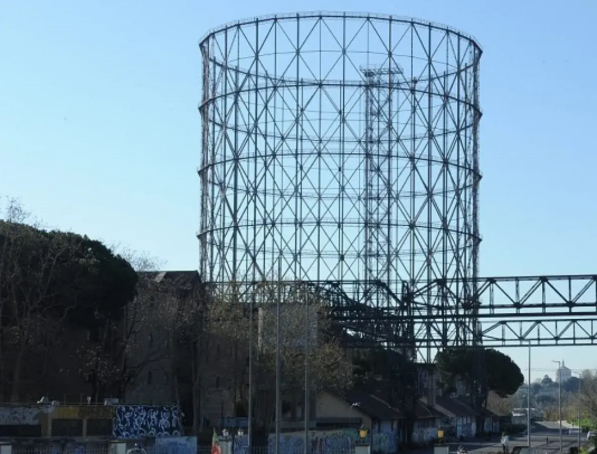 Il **gasometro Roma** si erge imponente contro il cielo azzurro, una struttura metallica iconica che domina il paesaggio urbano.