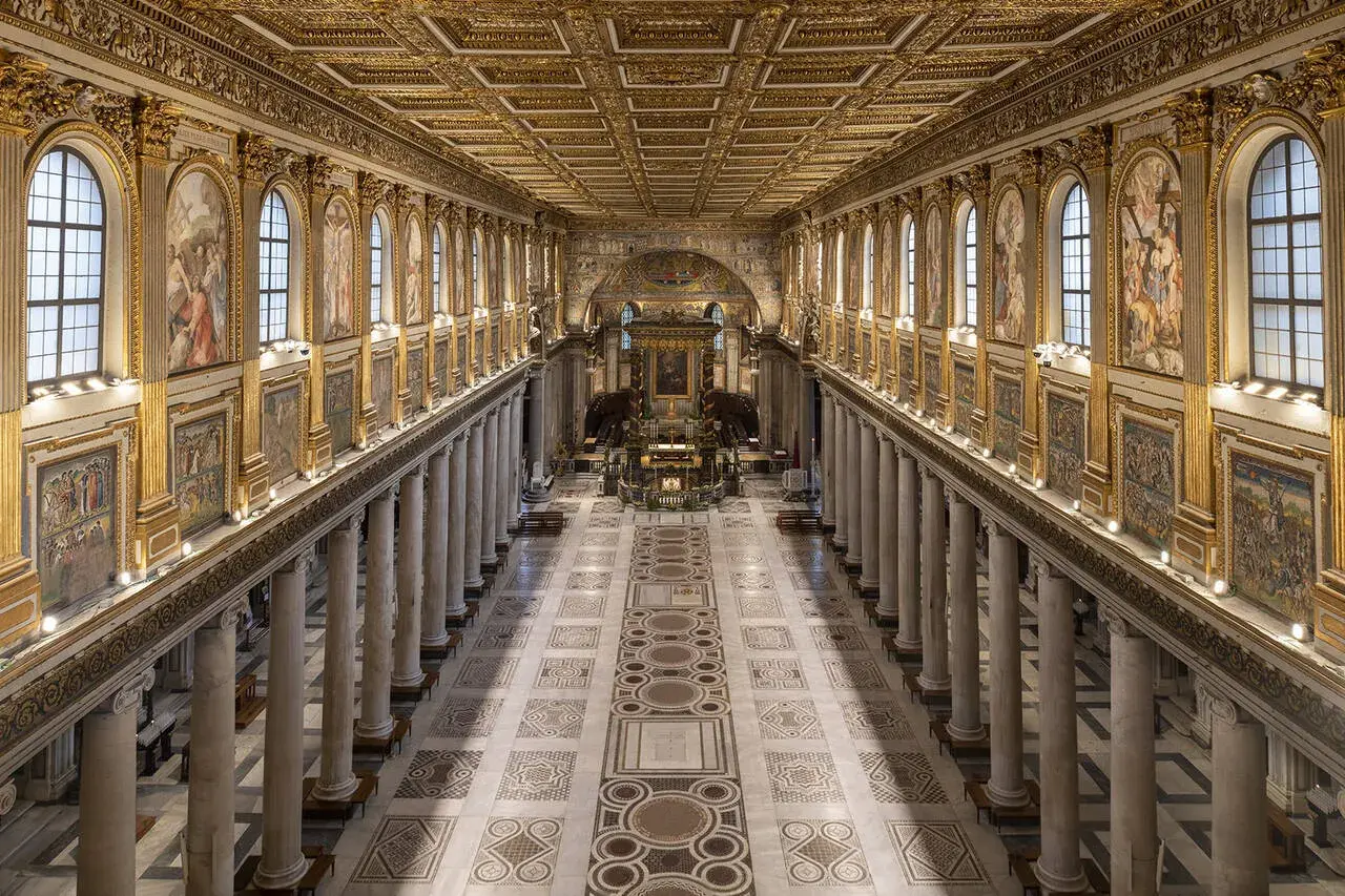 L'interno della Basilica di Santa Maria Maggiore a Roma, con il suo soffitto dorato, le colonne imponenti e i mosaici che narrano storie sacre.