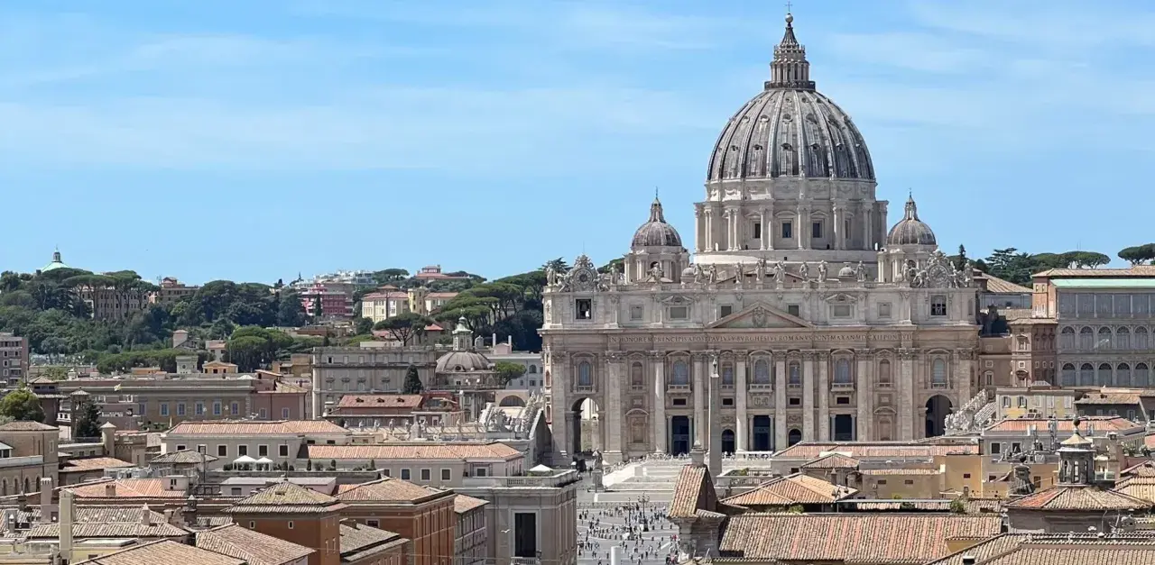 Vista panoramica di Roma con la Basilica di San Pietro in primo piano. Si intravedono i tetti della città e il cielo azzurro. Vicino alla stazione Ottaviano, un luogo iconico.