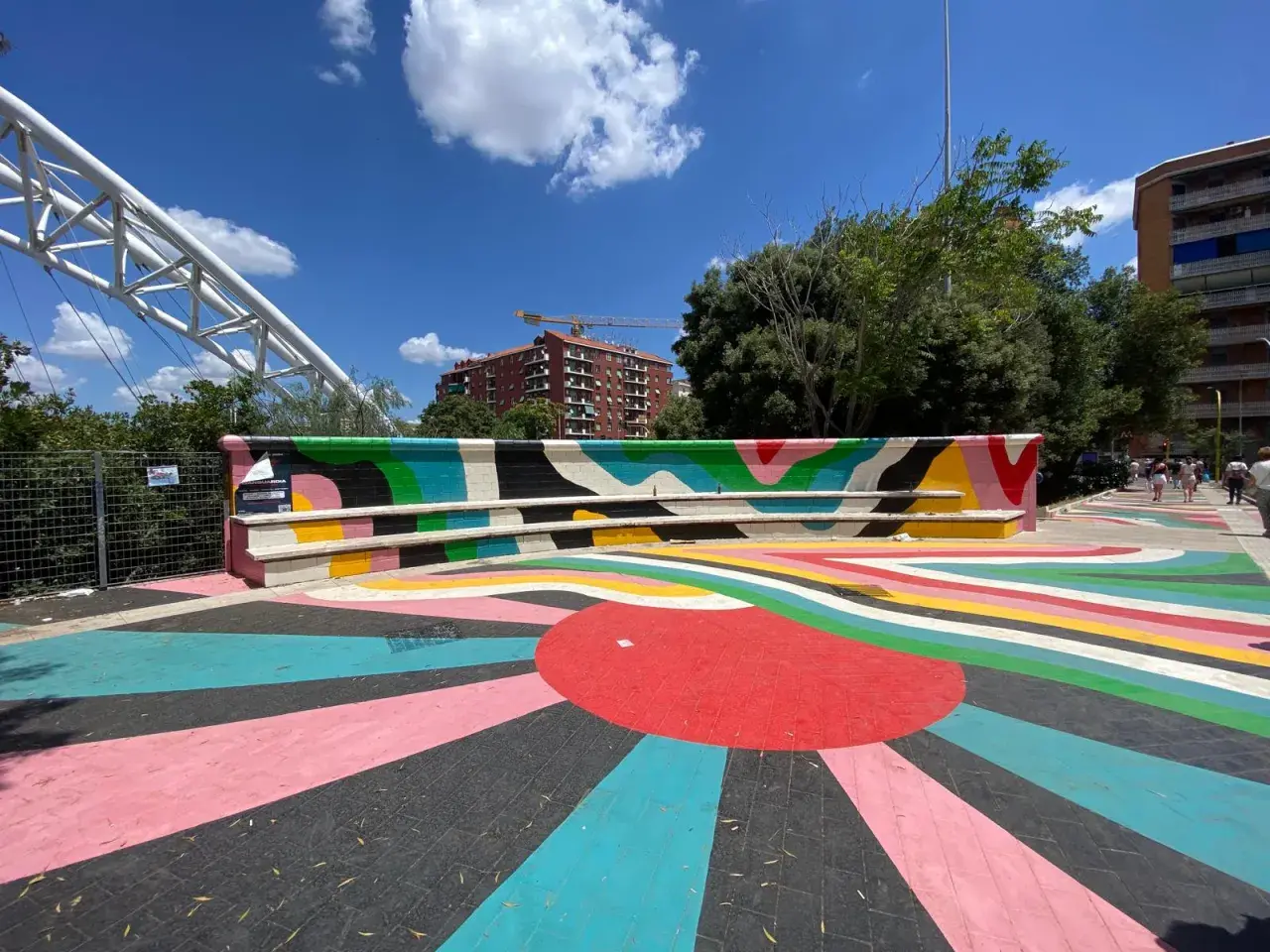 Piazza colorata vicino alla metro Garbatella a Roma, con un murale vivace e un grande sole stilizzato sul pavimento.