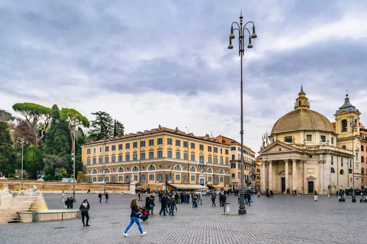 Piazza del Popolo a Roma a novembre, con la chiesa gemella e il palazzo giallo sotto un cielo nuvoloso.