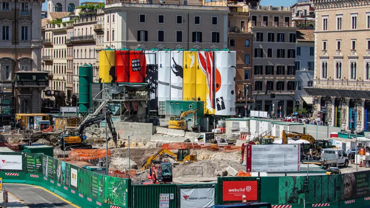 Cantiere per i lavori metro Roma con grandi teli colorati e macchinari edili.