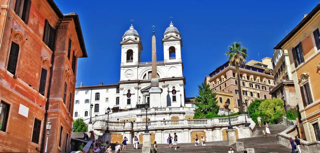 La scalinata di Trinità dei Monti a Roma, con la chiesa e l'obelisco sotto un cielo azzurro.