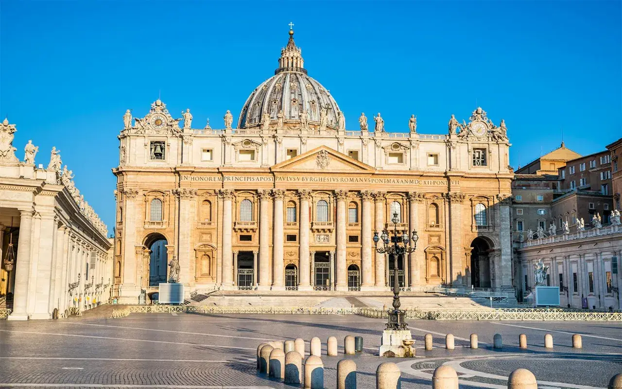 La maestosa basilica di San Pietro, un'antica meraviglia architettonica, domina la piazza con la sua imponente cupola sotto un cielo azzurro.