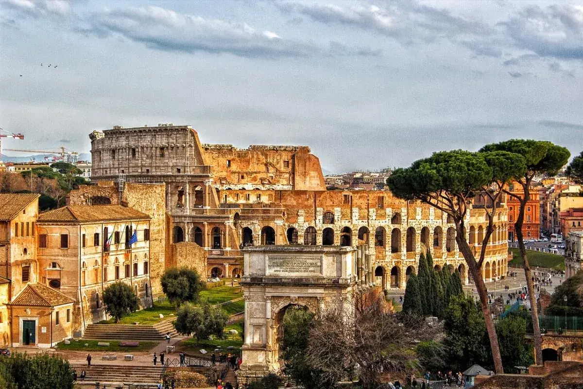 Colosseo e Arco di Tito, un'idea di cosa vedere a Roma in un giorno gratis, con pini romani e cielo nuvoloso.