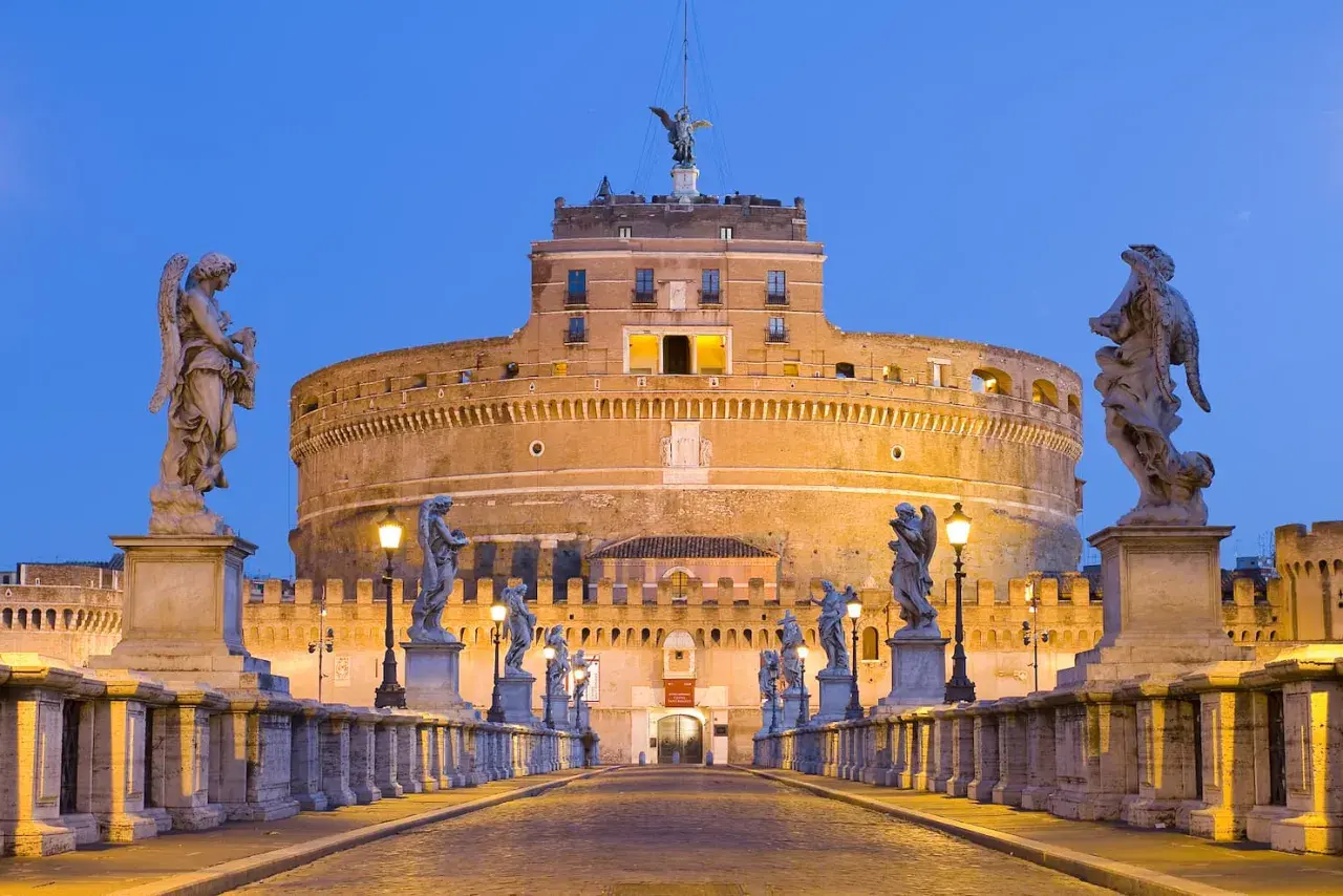 Ponte Sant'Angelo illuminato di sera, con le statue degli angeli e Castel Sant'Angelo sullo sfondo. Curiosità: la statua in cima al castello.