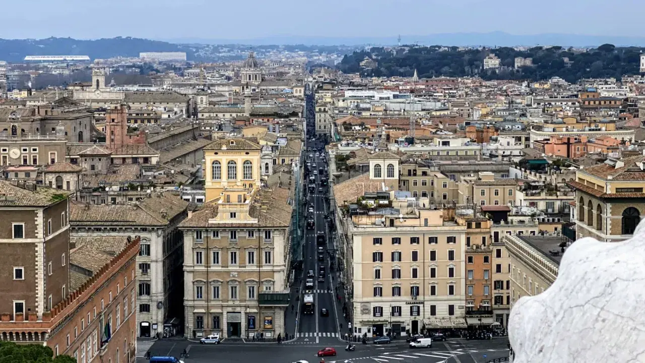 Vista aerea di Roma con traffico su Via del Corso. Edifici storici e tetti si estendono all'infinito.