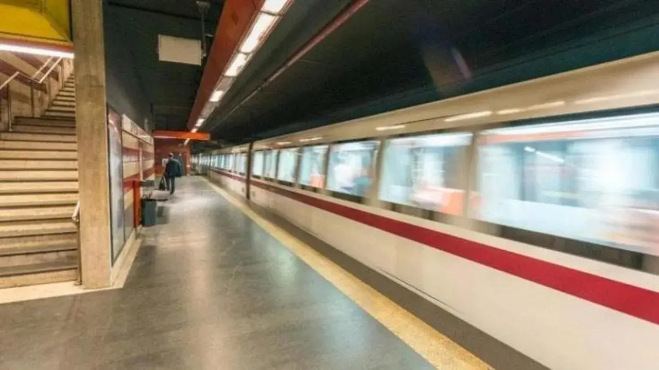 Treno in corsa su binari di una stazione metro. Si intravedono scale e un passeggero in attesa. Le fermate metro a Chiuse sono un luogo di passaggio frenetico.