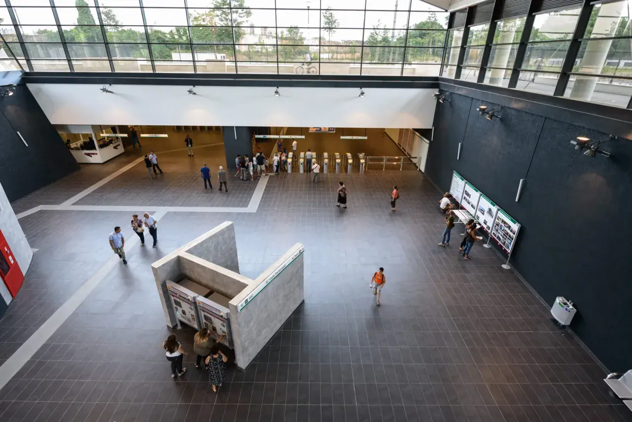 Interno moderno della fermata Teano metro C, con persone che acquistano biglietti e si dirigono verso i tornelli.