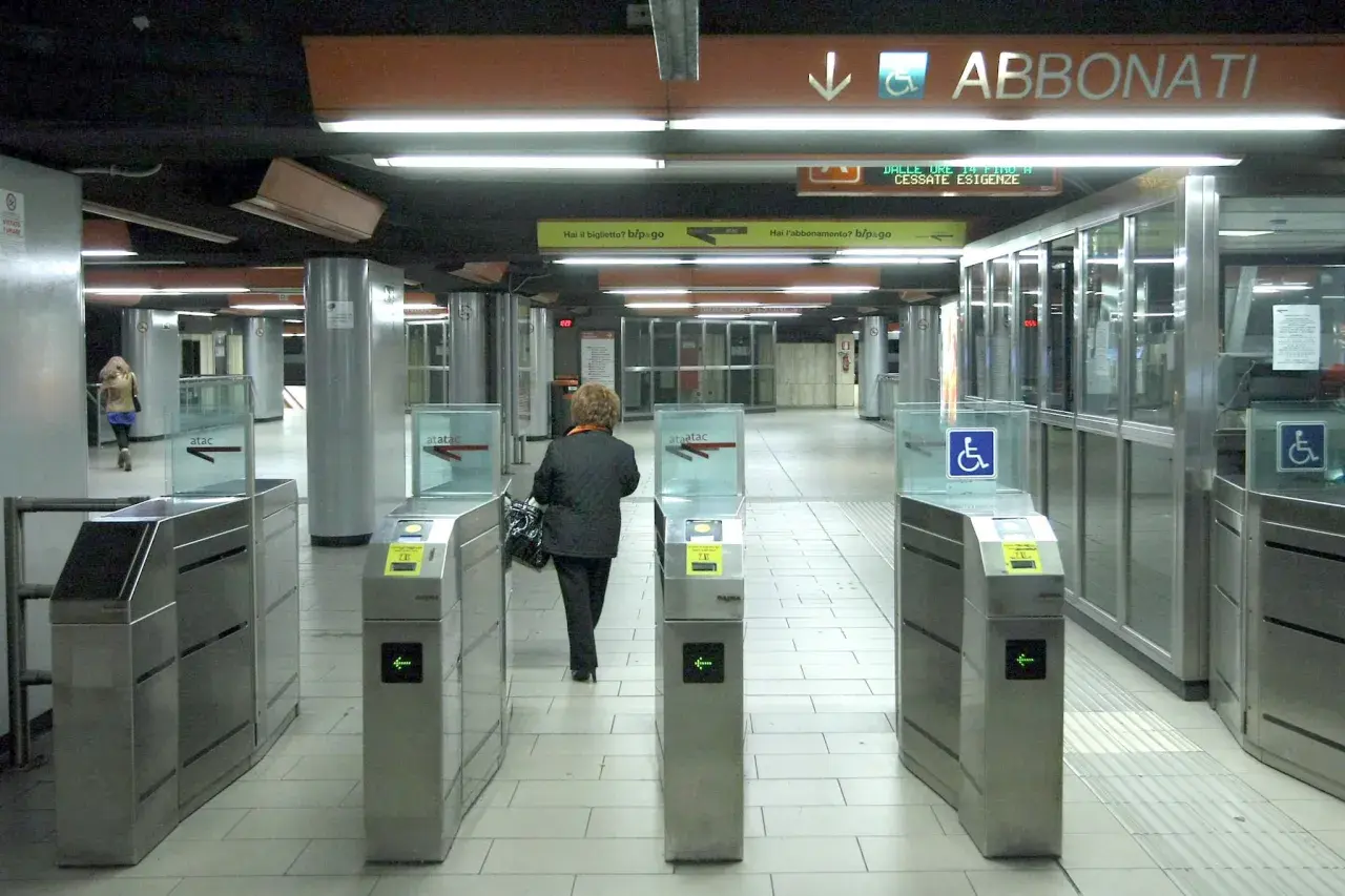 Ingresso della metropolitana di Roma con tornelli ATAC. Una donna attraversa i varchi per accedere ai binari.